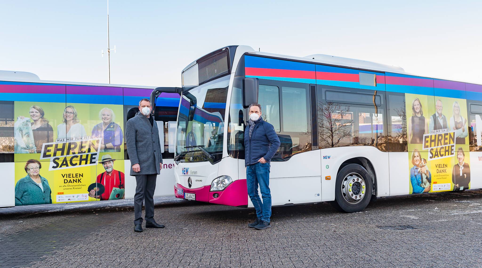  Landrat Dr. Andreas Coenen und NEW-Betriebsleiter Uwe Peters vor den beiden Bussen, die mit Fotos von Ehrenamtlichen aus dem Kreis beklebt sind.  