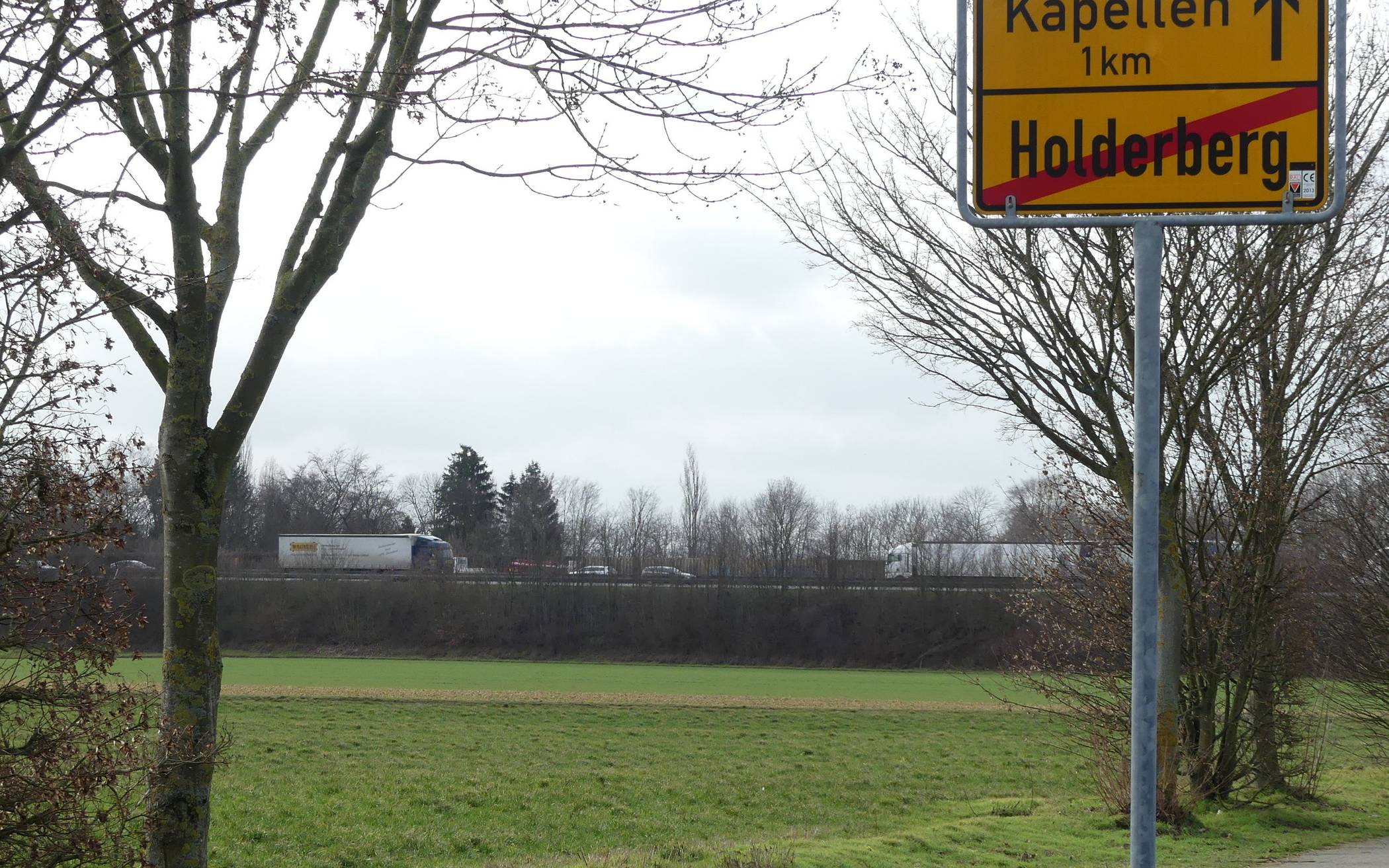 Ortsausgang Holderberg, Wilhelm-Anlahr-Straße, im Hintergrund die Autobahn. Beim Ausbau ist von der Brücke bis zum Grafschafter Rad- und Wanderweg keine Lärmschutzwand geplant. Derzeit befahren die A57 im Bereich Kapellen etwa 76.000 Fahrzeuge pro Tag. Für das Jahr 2030 ist ein Verkehrsaufkommen von rund 81.000 Fahrzeugen je Tag prognostiziert. 