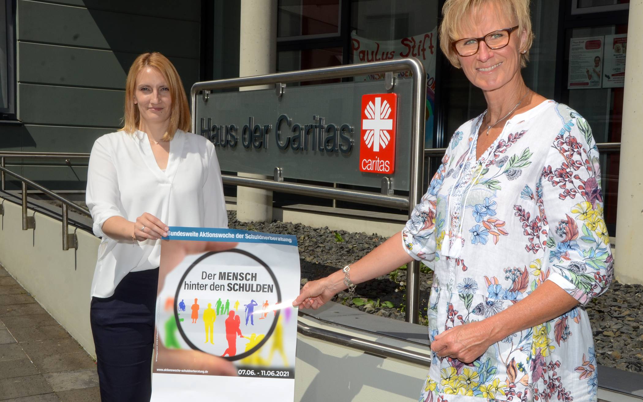 Für die Schuldnerberatung der Caritas zählt der „Mensch hinter den Schulden“. Bereichsleiterin Annika Schuhmacher (l.) und Schuldnerberaterin Elisabeth Mankertz mit dem Plakat der Aktionswoche. Foto: Caritasverband