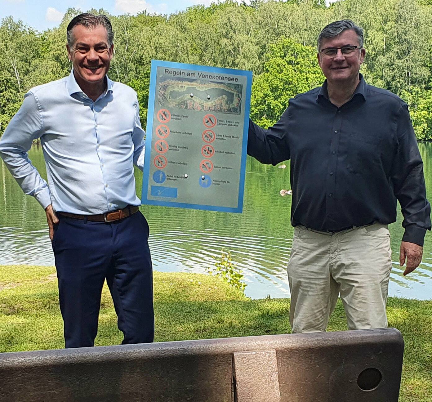   Die Bürgermeister von Brüggen und Niederkrüchten, Frank Gellen und Karl-Heinz Wassong (v.l.), präsentieren die Schilder mit den neuen Regeln für Venekoten- und Dahmensee. 