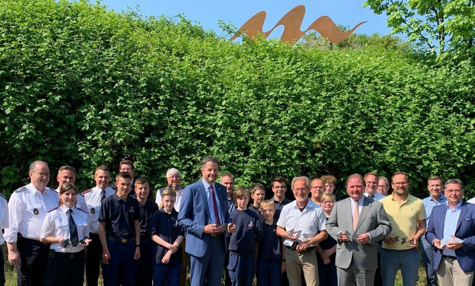 Und über allem schwebt die Welle: Bürgermeister Christian Bommers, Michael Heinze und Finanzminister Lutz Lienenkämper (Mitte vorn) übergaben mit Vertretern der Jugendfeuerwehr, Unterstützern und Sponsoren jetzt auch offiziell die Meerbusch-Skulptur an der A57. 