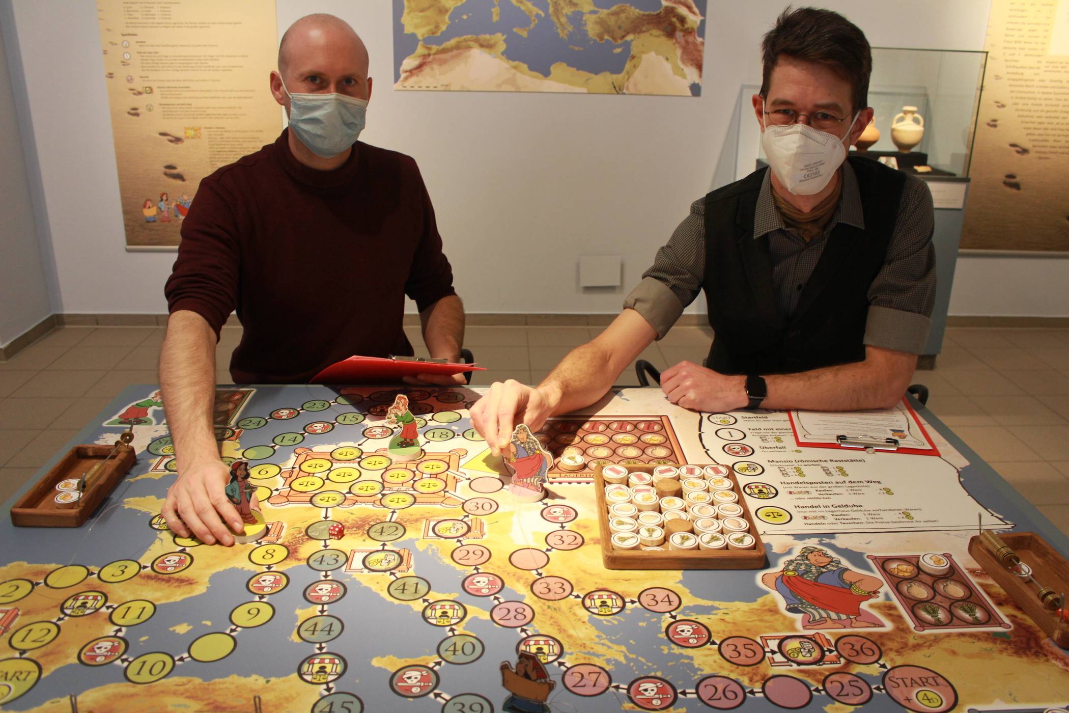  Amüsant: Im Archäologischen Museum an der Rheinbabenstraße hat Museumspädagoge Matthias Ackermann (r.) das selbst erfundene Brettspiel zur Sonderausstellung "Heimat in der Fremde" aufgestellt. Jeder Besucher  kann es einfach spielen. Zusammen mit Doktorand Eric Sponville (l.) spielt es der Erfinder auch selber gern. Zum „Limes-Sonntag“ ist unter freiem Himmel auch eine Outdoor-Version des Spiels aufgebaut. Es versetzt die Spieler in die Rollen römischer Händler. Foto: Müller 