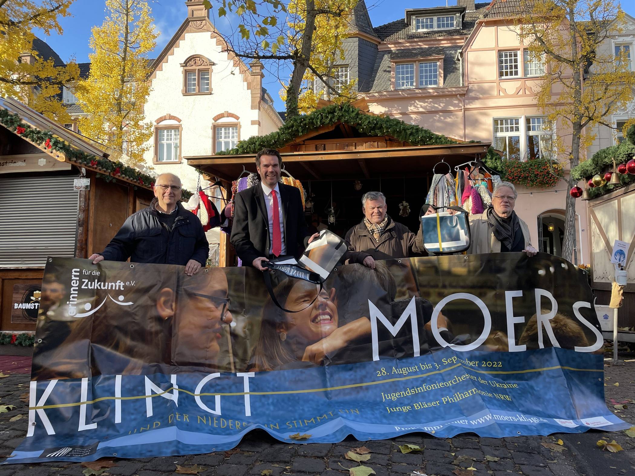 Ulrich Hecker (Erinnern für die Zukunft), Stefan Ertl (Sparkasse am Niederrhein), Rainer Tyrakowski-Freese (Tuwas Genossenschaft eG) und Konrad Göke (organisatorischer Leiter MOERS KLINGT) präsentieren einen der noch unverarbeiteten Banner und die Taschen, die es am Montag auf dem Weihnachtsmarkt gegen eine Spende von mindestens 20 Euro zu erwerben gibt. 
