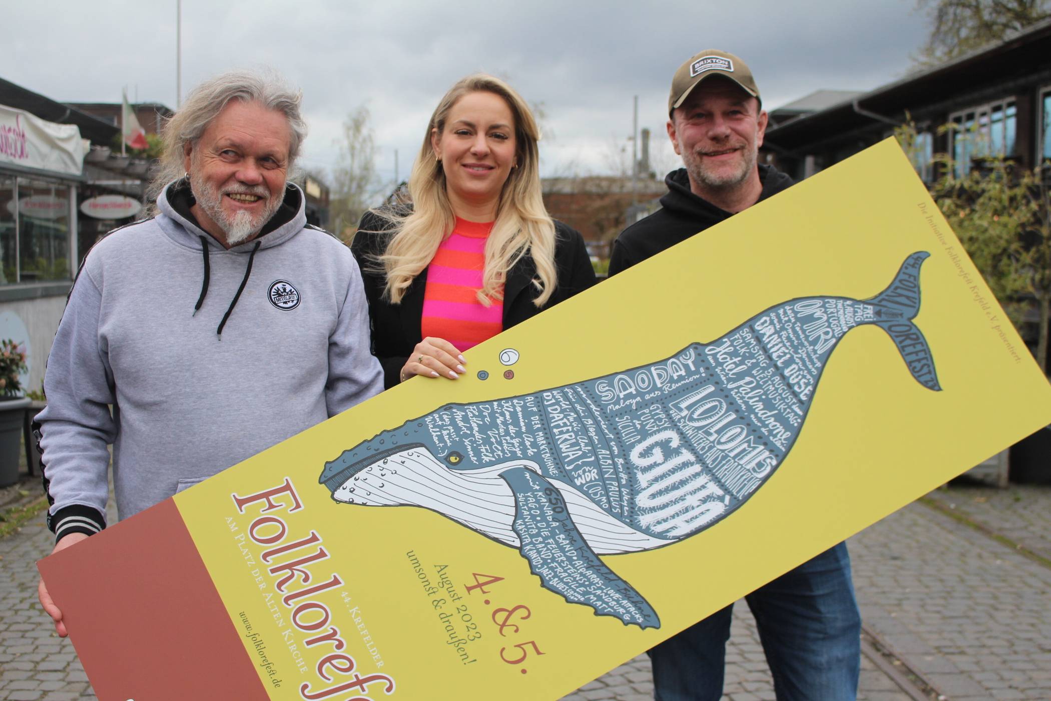  Präsentieren zum Folklorefest das neue Mottoplakat mit Buckelwalmotiv: (v.l.) Programmplaner Jordi Preußer, Sprecherin Jennifer Kuhnes und Platzverantwortlicher Michael Spatz von der Initiative Folklorefest Krefeld e.V.   