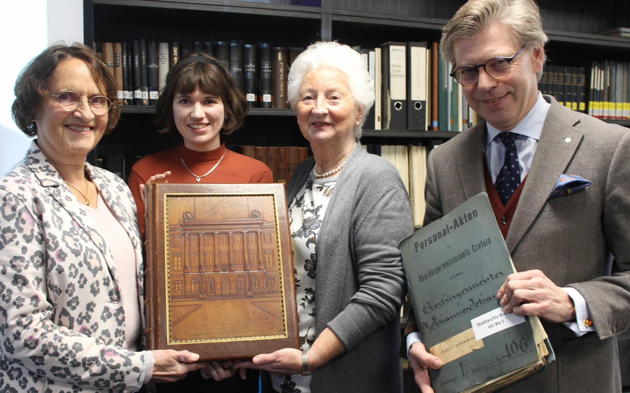  Präsentieren das schwere Fotoalbum mit Prägung des Krefelder Rathauses: die Stifterinnen Renate Rommel-Hohneck (l.) und Roswita Engels (r.) sowie Archivmitarbeiterin Fenja Schneiders. Archivleiter Dr. Olaf Richter hat passend dazu die Personalakte des ehemaligen Besitzers Johannes Johansen aus dem Magazin geholt.  