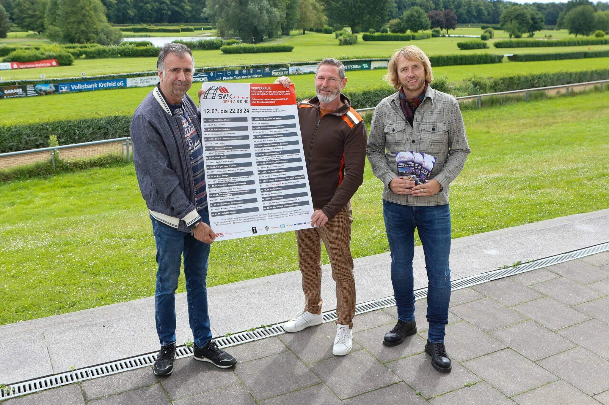 Vor der grünen Kulisse der Rennbahn präsentieren Volko Herdick, Michael Paßon und Uwe Papenroth das neue Programm des SWK Open Air Kinos. 