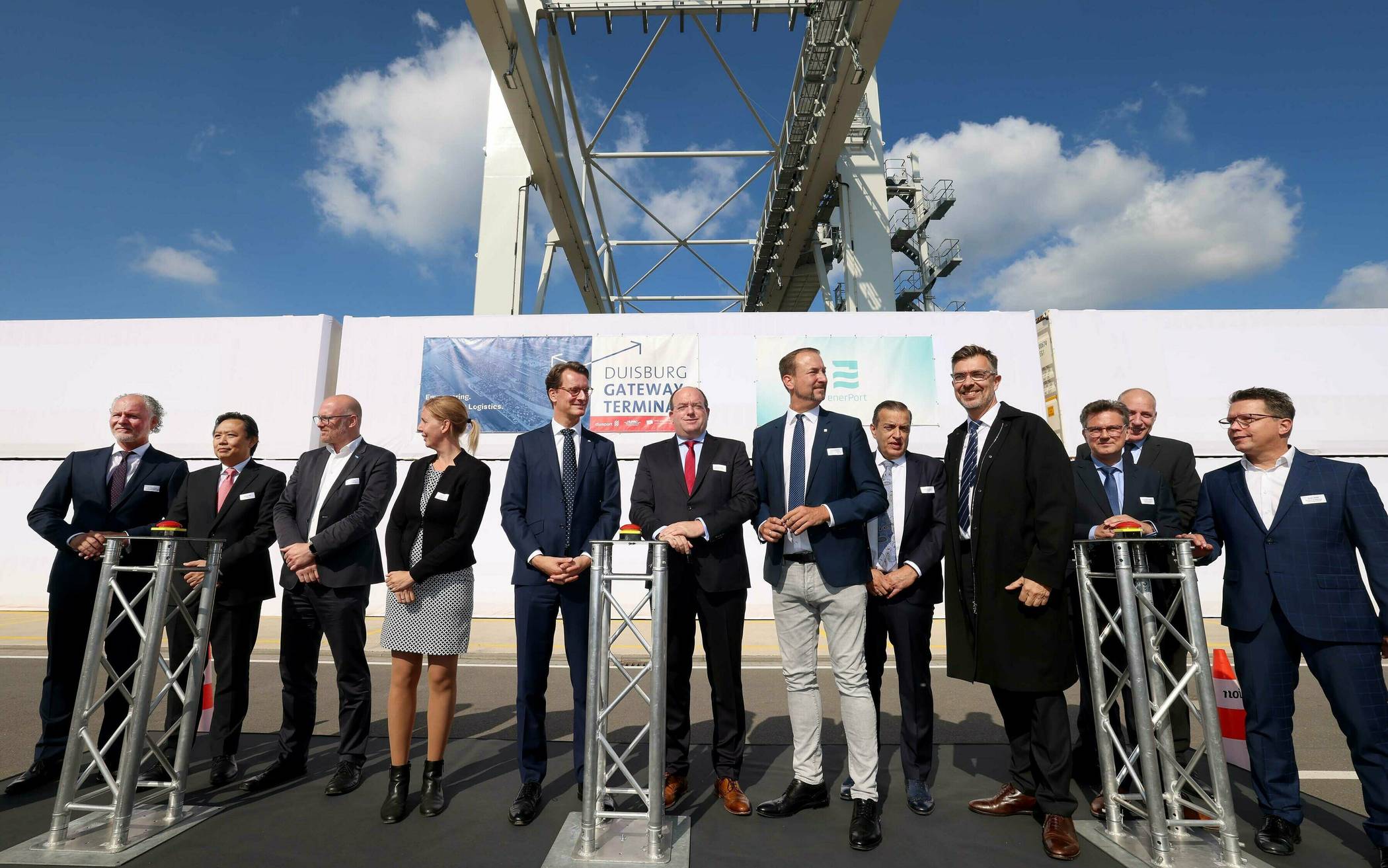  ... eingeschwenkt wird der „Grundsteincontainer“ vor Ministerpräsident Wüst, Hafenchef Bangen (5. u. 6. v. l.) und den internationalen Projektpartnern. 