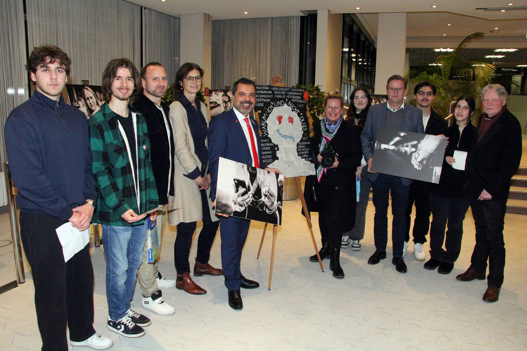 Ausstellungseröffnung in der Kundenhalle der Sparkasse am Ostring: Giovanni Malaponti, der Vorstandsvorsitzende der Sparkasse am Niederrhein (links), und Marc Inderfurth, Vorstand des Caritasverbandes Moers-Xanten, halten je eines der ausgestellten Fotos von Bettina Engel-Albustin (Mitte) in der Hand. Vera Michael, Schulleiterin der Anne-Frank-Gesamtschule, und SV-Lehrer Sebastian Abel (4. Und 3. v.l.) waren mit einigen Schülern gekommen, die eigene Texte lasen. Ganz rechts: Konrad Göke, der die Lesung mit den Schülern einstudiert hatte. 