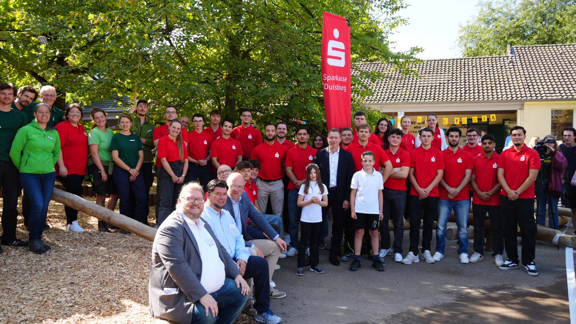 Auf dem Foto zu sehen sind (v.l.n.r.): die Mitarbeiter und Mitarbeiterinnen der Alea GmbH, die Auszubildenden und das Ausbildungsteam der Sparkasse Duisburg (in Rot gekleidet), Daniel Gierhartz (Vorstand des Fördervereins der GGS Marienstrasse, Erik Klein (Schulleiter der GGS Marienstraße), Oberbürgermeister Sören Link und Vorstandsmitglied Marcus Budinger.