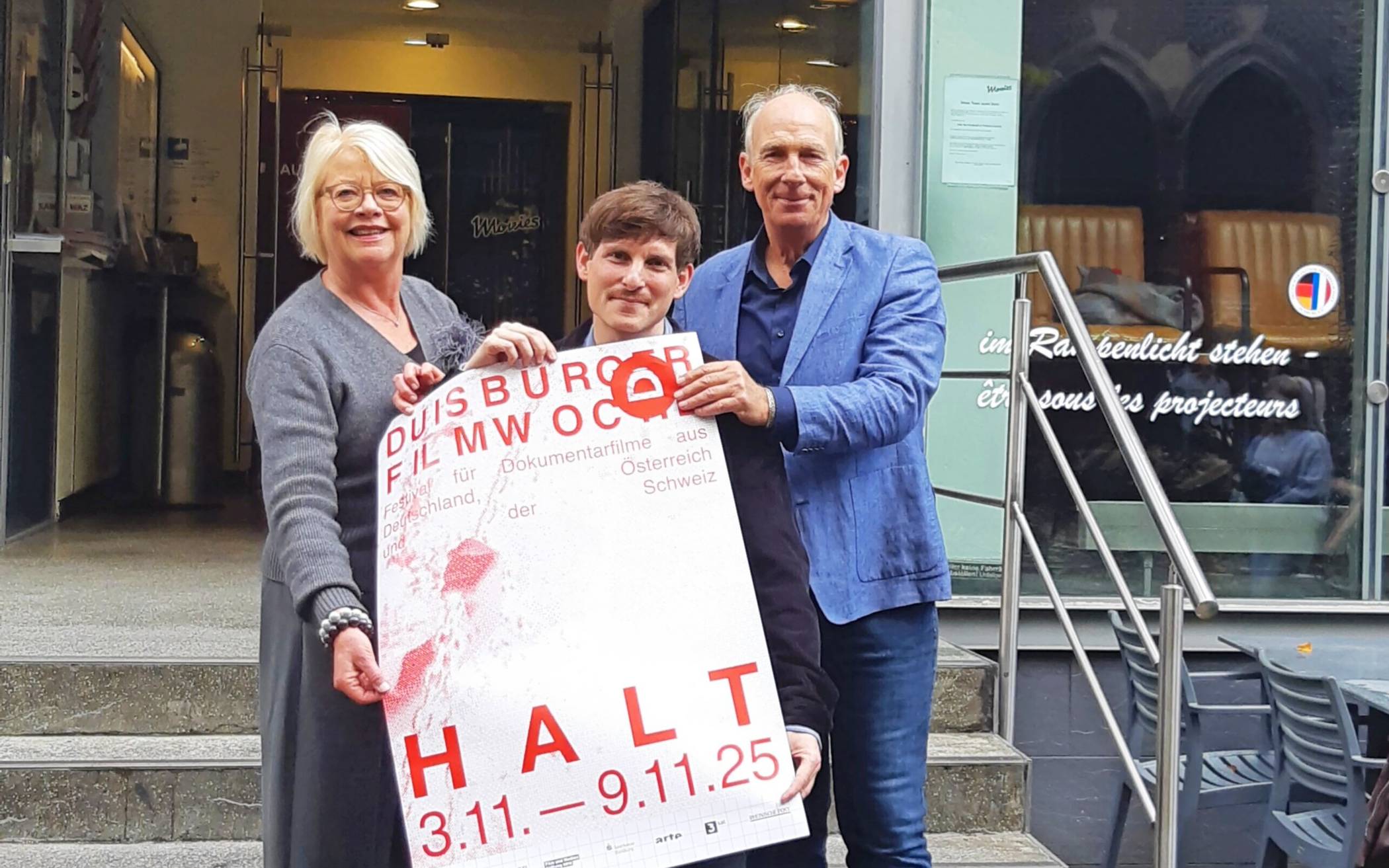  Kulturdezernentin Astrid Neese, Filmwochenleiter Alexander Scholz und Vhs-Leiter Volker Heckner mit dem Filmwoche-Plakat vorm Filmforum 
