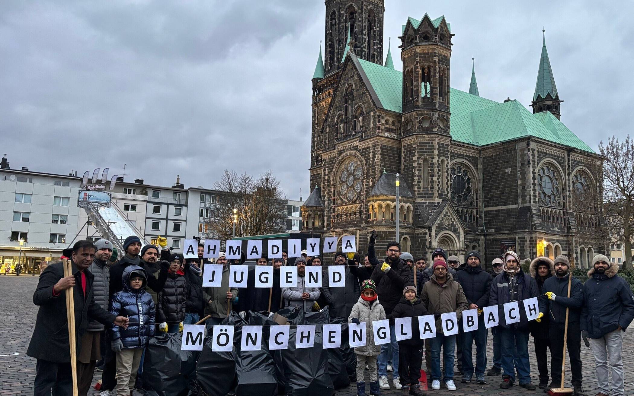 Die Neujahrsaktion der Ahmadiyya Muslim Gemeinde in Mönchengladbach verbindet bewusst spirituelle Motivation mit praktischem bürgerschaftlichem Engagement: Sie beginnt als gemeinsames Zeichen der Dankbarkeit und des Friedens und wird unmittelbar in eine konkrete, sichtbare Tat für das Gemeinwohl überführt. Ziel der Aktion ist es, das neue Jahr mit einer positiven, konstruktiven Geste zu eröffnen, das Stadtbild zu verschönern, Verantwortung für den öffentlichen Raum zu übernehmen und durch unaufdringliche Hilfe das Vertrauen und den Zusammenhalt in der Nachbarschaft zu stärken. Indem Gemeindemitglieder aktiv Müll beseitigen, senden sie ein klares Signal für Rücksichtnahme, Sauberkeit und respektvolles Miteinander, das über rein symbolische Wirkung hinausgeht.  Der Ablauf der Aktion ist klar strukturiert und zugleich gemeinschaftlich getragen: Der Tag beginnt mit einem gemeinsamen Gebet, das die Motivation als Ausdruck von Dankbarkeit und dem Wunsch nach Frieden für das neue Jahr rahmt. Anschließend machen sich die Teilnehmenden – in diesem Jahr 35 Mitglieder – mit Handschuhen, Greifzangen und Müllsäcken auf den Weg zum Marktplatz. In koordinierten Kleingruppen werden Wege, Plätze und Sitzbereiche systematisch abgesucht; innerhalb kurzer Zeit füllen sich mehrere Säcke mit Feuerwerksresten, Flaschen, Verpackungen und anderem Abfall. Die Arbeit verläuft effizient, sodass bereits während der Aktion eine deutliche Verbesserung des Stadtbildes sichtbar wird.  Am Ende steht nicht nur ein sauberer Marktplatz, sondern auch eine gestärkte Gemeinschaftserfahrung: Die Teilnehmenden erleben, wie gemeinsames Handeln unmittelbare Wirkung entfaltet, und die Aktion erzeugt positive Resonanz bei Anwohnern und Vorbeigehenden. Langfristig zielt die Initiative darauf ab, Vorurteile abzubauen, Dialogbereitschaft zu signalisieren und andere zu inspirieren, Verantwortung für den öffentlichen Raum zu übernehmen. So wird aus einem einfachen Neujahrsputz ein Beitrag zu einem respektvollen, vernetzten und lebenswerten Mönchengladbach.