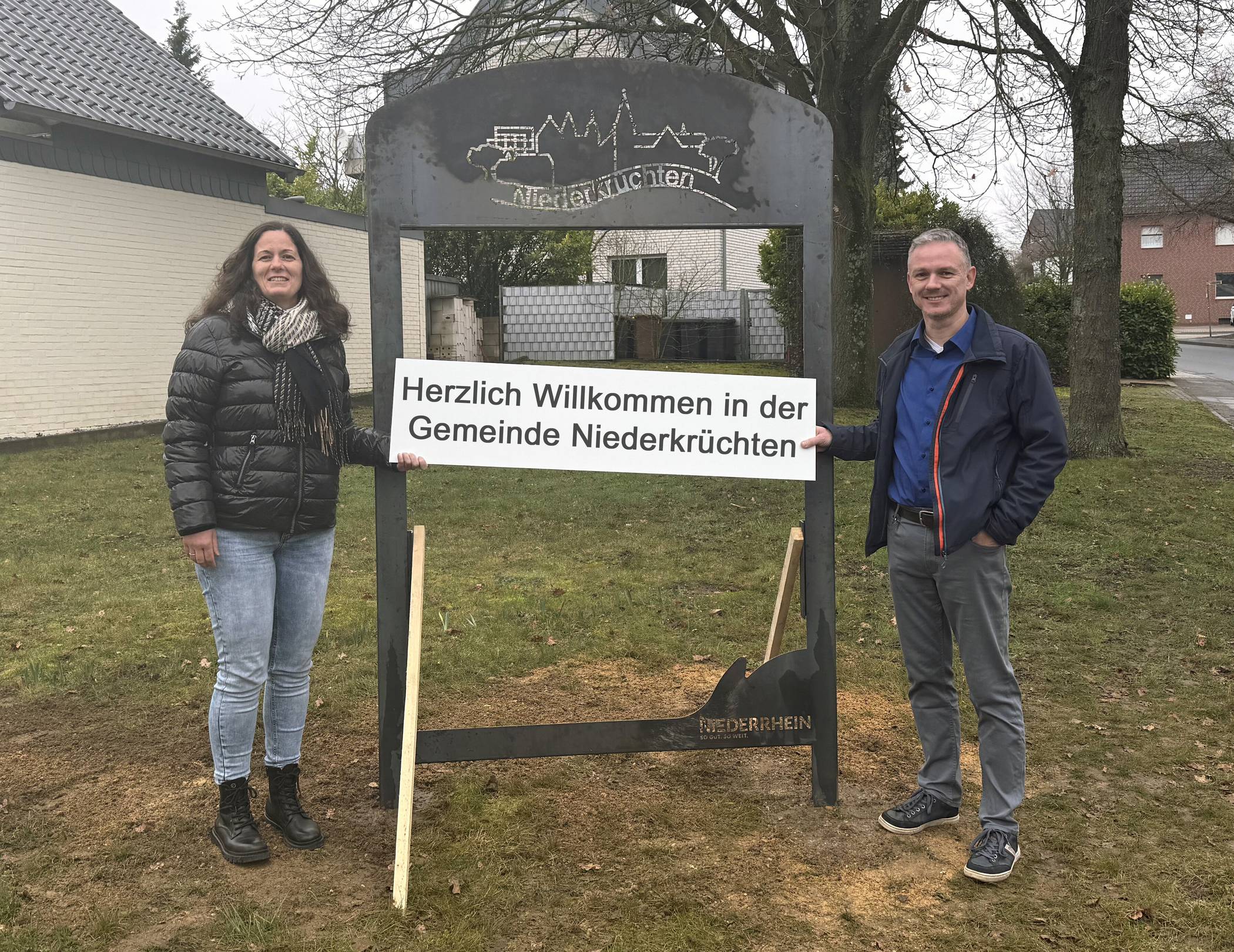 Svenja Sonnemans und Frank Grusen vor einem der sechs neuen Schilder, an denen künftig Veranstaltungen in der Gemeinde angekündigt werden.  