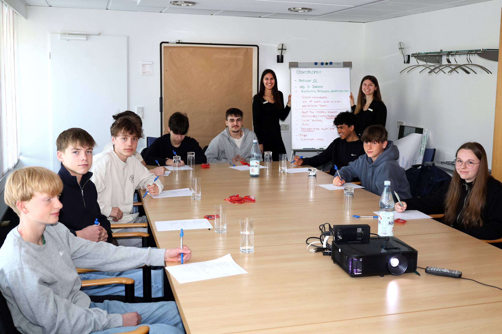 Neun Neuntklässler des Amplonius-Gymnasiums erfuhren im Seminarraum der Sparkasse an der Bahnhofstraße in Rheinberg, warum grundlegendes Finanzwissen fürs Leben enorm nützlich ist. Lilly Berner (hinten links) und Viviana Polotzek (rechts daneben) informierten zudem über die verschiedenen Tätigkeitsbereiche von Bankkaufleuten und berichteten von ihrem vielseitigen Berufsalltag.