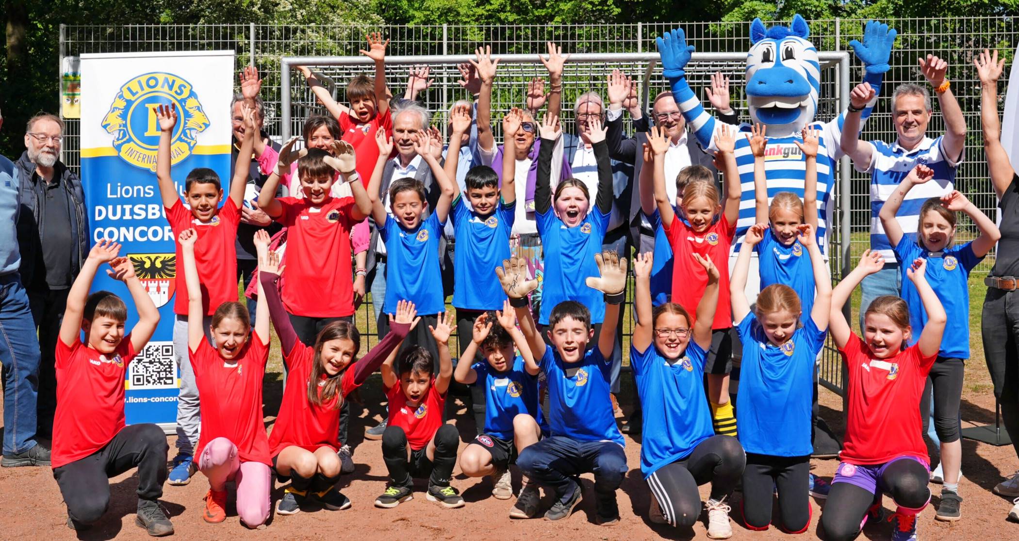 Team Rot und Team Blau mit Lehrerin Gila Wittig, Bernard „Ennatz“ Dietz, Maskottchen Ennatz und MSV-Chef Christian Stiefelhagen, Oberbürgermeister Sören Link, WBD-Chef Thomas Patermann, Tanja Bock vom Lions-Club Duisburg Concordia, Rheinhausens stellvertretender Bezirksbürgermeister Ferdi Seidelt feiern den runderneuerten Bolzplatz an der Breslauer Straße. 