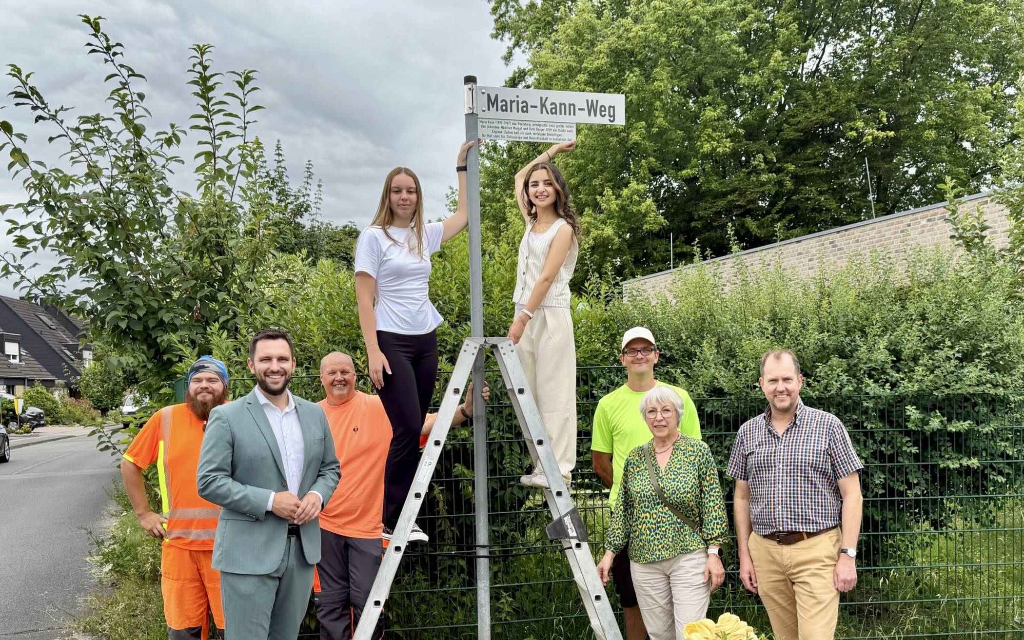 Die Schülerinnen Nadja Gerten (links auf der Leiter) und Afrah Girdo befestigten das Schild. Mit dabei (v.l.): Marc Abicht (DLB), Bürgermeister Philipp Richter, Michael Stülpner (DLB), Stadtarchivarin Sabine Sweetsir, Heiko Wehr (Fachbereich Tiefbau) und Thomas Ververs, Lehrer an der Europaschule Rheinberg. 