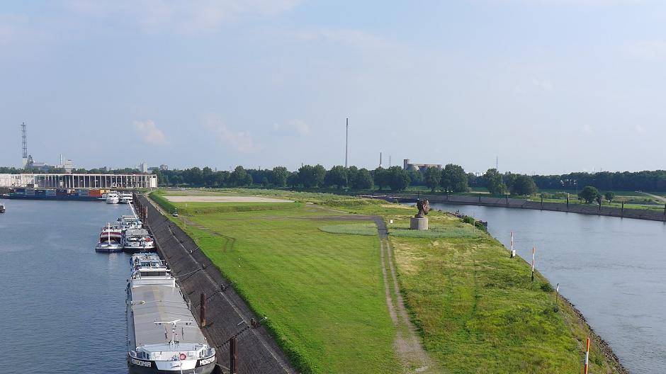 Im Vordergrund die Rampe zur Treppe auf die Homberger Brücke, ganz im Hintergrund der Rohbau der ersten Logistikhalle. Das Parkgelände wird sich von der Rampe aus bis etwas hinter die Poseidon-Skulptur erstrecken.