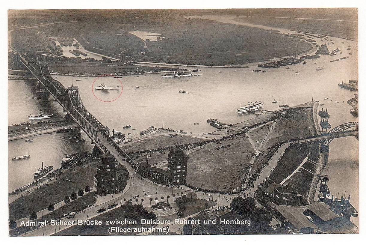 Luftbild des Ereignisses aus Ruhrorter Perspektive mit der alten Admiral-Scheer-Brücke (heute Friedrich-Ebert-Brücke) und tausenden Schaulustigen. Die Dornier-X (roter Kreis) liegt auf Höhe des Rheinpreußenhafens auf Homberger Seite.
