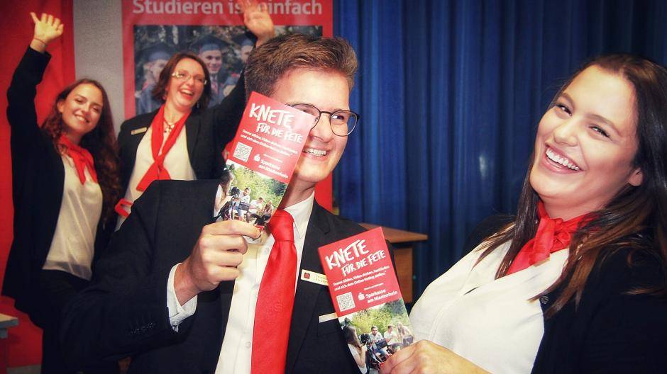 Die Azubis Fernando Escudero und Kathrin Müller zeigen die Flyer zum Video-Wettbewerb „Knete für die Fete“. Bereits zum fünften Mal lobt die Sparkasse am Niederrhein Party-Zuschüsse von 1.000, 750 und 500 Euro für die Abschlussjahrgänge von weiterführenden Schulen aus. Lara Ena und Christine Heinrichsmeyer (hinten) hätten da schon ein paar lustige Ideen fürs Drehbuch.