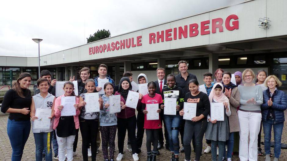  Strahlende Gesichter an der Europaschule: 21 Flüchtlingskinder bestanden die Sprachprüfung der VHS. Ganz links: Hülya Atasoyi, ganz rechts: Elisabeth Keggenhoff und (3.v.r.) Elke Vasel. Martin Reichert (10.v.r.) und Tim Rütters (links daneben) hatten zuvor die Zertifikate überreicht. 