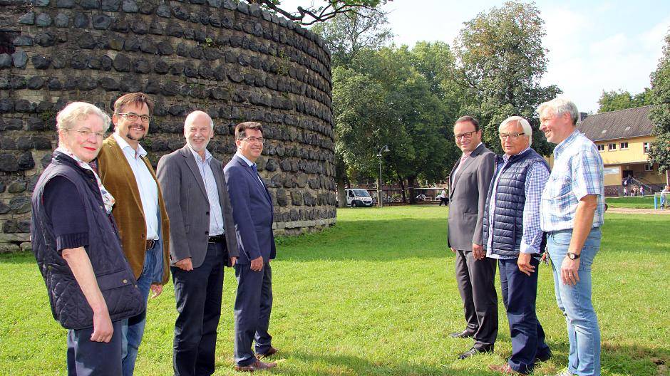 Bettina Raendchen und Ralf Winstroth von der Bürgerinitiative, Baudezernent Dieter Paus, Bürgermeister Frank Tatzel, Sparkassenvorstand Frank-Rainer Laake sowie Viktor Vervoort und Jupp Böckling stehen Spalier für die Laterne mit den zwei Strahlern (im Hintergrund), die den Platz am Pulverturm abends beleuchten.