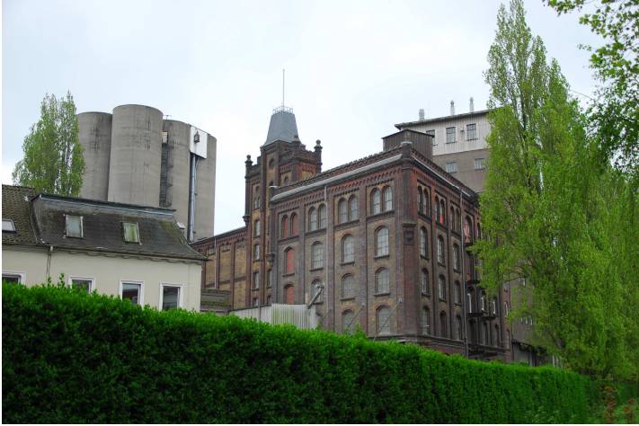  Auf diesem Foto ist der Kontrast zwischen dem schlossartigen Mühlengebäude von 1904/06 und den industriemodernen Silobauten von 1936/39 gut verdeutlicht. Die zylindrischen Silos am Rhein sind aus den 1980er Jahren. Die denkmalwürdigen sind in dem quadratischen Klinkerbau im Hintergrund untergebracht. 