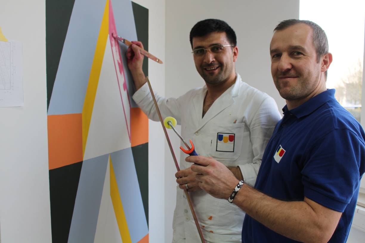  In der Ausbildungswerkstatt der Malerinnung: Asylbewerber Khaled Alrime (l.) hat schon nach kurzer Anleitung ein farbenfrohes und exakt ausgemessenes Muster an die Übungswand gemalt. Ausbildungsleiter Sascha Zester ist freudig erstaunt über die Fertigkeit seines Schülers. 