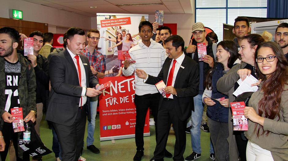 Azubi Raphael Gaitanis (l.) und Vorstandsvorsitzender Giovanni Malaponti verteilen Flyer für den Videowettbewerb der Sparkasse an Schülerinnen und Schüler von Abschlussjahrgängen. „Knete für die Fete“ geht in die 3. Runde. Zu gewinnen gibt es Party-Zuschüsse von 1.000, 750 und 500 Euro.