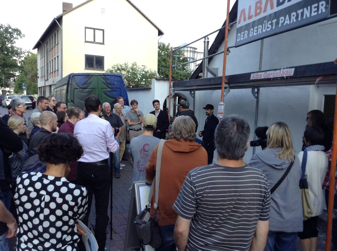  Bei der Besichtigung der Fassade entstand kurzerhand ein Nadelöhr. Die Neugierigen lauschen bespannt den Künstlern, da war der Nachmittagsverkehr auf der Kolpingstraße egal. 