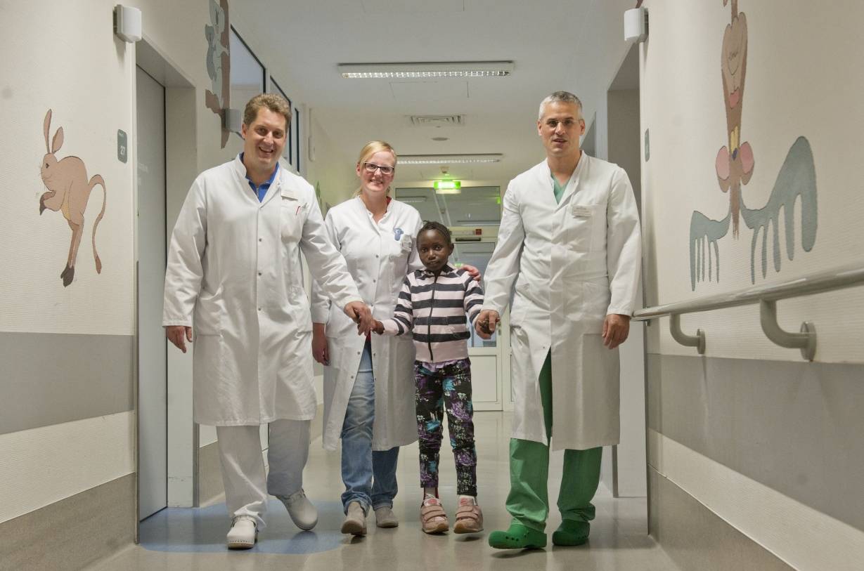 Das Laufen klappt jetzt ziemlich gut: Die neunjährige Patientin Oumie Kanteh aus Gambia freut sich, nach einem Dutzend Operationen wieder nach Hause fliegen zu können. In Bethanien hatten der über die Region hinaus bekannte Wiederherstellungschirurg Prof. Dr. Robert Hierner (re.), KIndertraumatologe Dr. Christian Illian (li.) und die Kinderkliniks-Oberärztin Dr. Sabine Labus (M.) die Patientin zwei Jahre lang in Moers betreut.