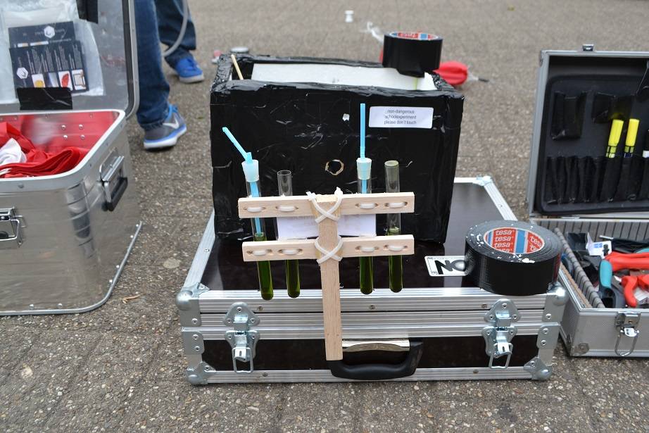  An der Box befestigt, die Reagenzgläser mit der Chlorophyll-Lösung aus Spinat und Alkohol. In der Box befinden sich Datenlogger und Kameras zur Dokumentation. 