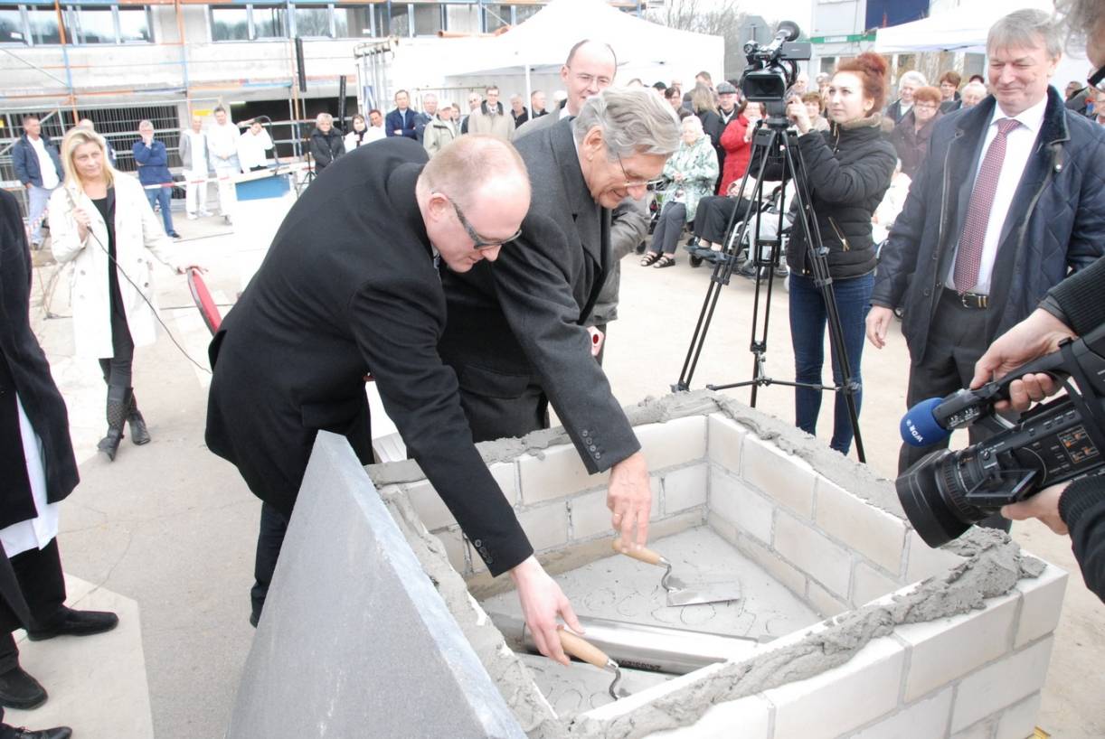 Ekkehard Schulz, Aufsichtsratsvorsitzender der Klinik, mauert gemeinsam mit Oberbürgermeister Sören Link die „Zeitzeichen-Rolle“ in den Grundstein.