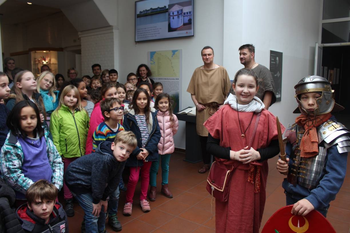  Großes Interesse: Die Kinder der Paul-Gerhard-Schule nahmen gestern am Starttag den neuen Info-Point mit Flachbildschirm und Info-Tafel unter die Lupe. Ralf Möller und André van de Bruck führten die Schüler in die Welt der alten Römer ein und brachten sogar echte Kostüme mit. Museums-Direktorin Dr. Jennifer Morscheiser (hinten Mitte) freute sich über so viel Eifer. 
