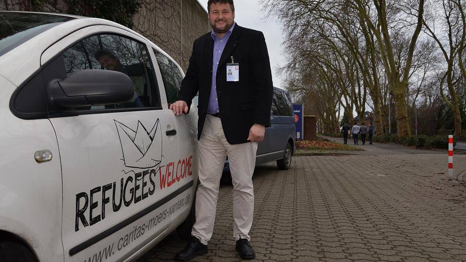 Henric Peeters ist Geschäftsführer des Caritasverbands Moers-Xanten. Vor der Kamp-Lintforter Landes-Notunterkunft steht er an einem Wagen, der mit dem Aufdruck „Refugees welcome“ Flüchtlinge ausdrücklich willkommen heißt.