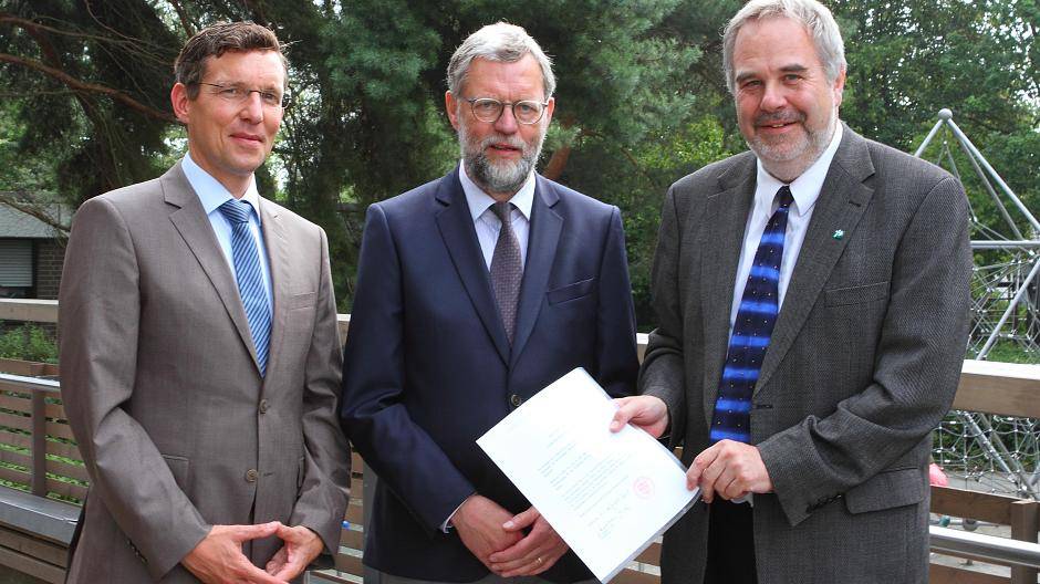  Offizieller Akt: Dr. Thomas Ervens (l.) und Rolf-Peter Cremer (r.) vom Generalvikariat Aachen überreichen Joachim Cuypers die Ernennungsurkunde zum Rektor der Maria-Montessori-Grundschule. 