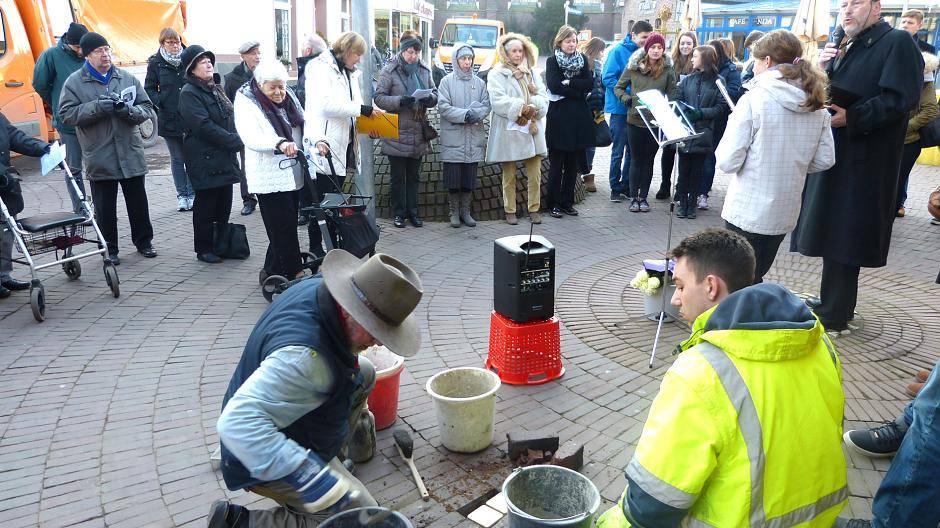 Gunter Demnig (vorne links) verlegt zwei Stolpersteine an der Bahnhofstraße. Hier lebten die Eheleute Henriette Defries und ihr Mann Simon. In der weißen Jacke mit Rollator ist Edith Bader-Devries zu sehen. Sie ist die Großnichte der Ermordeten.