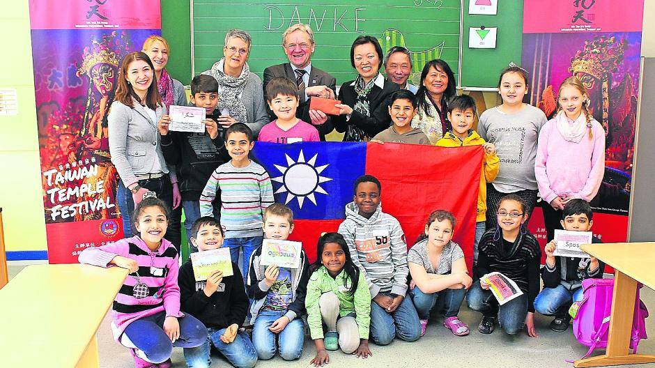 Dr. YANG Ying-Feng, LIN Hanbin und CHEN Lili von der Taiwangemeinde übergeben in der Grundschule am Mühlenfeld in Willich Bürgermeister Josef Heyes 3 177,93 Euro für die Arbeit mit Flüchtlingskinder. Die Schüler bedankten sich hierfür auf arabisch, kurdisch, russisch, armenisch und deutsch (kleine Schilder, die sie hochhalten).