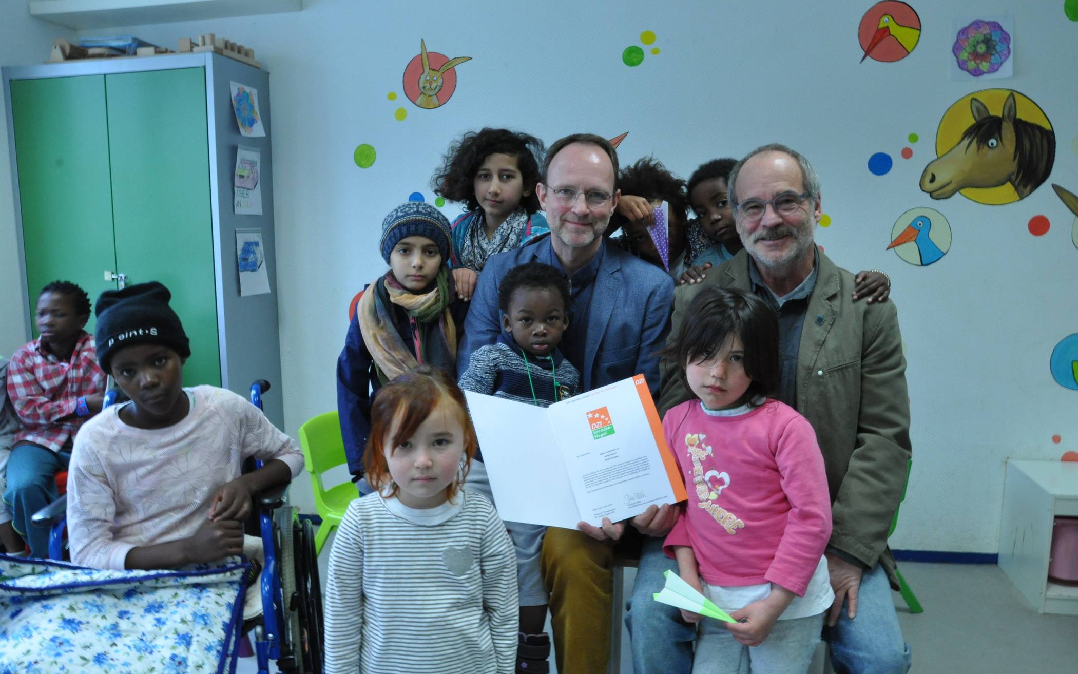 Burkhard Wilke (links) übergibt, umringt von Friedensdorf-Kindern, das DZI-Spenden-Siegel an Thomas Jacobs.