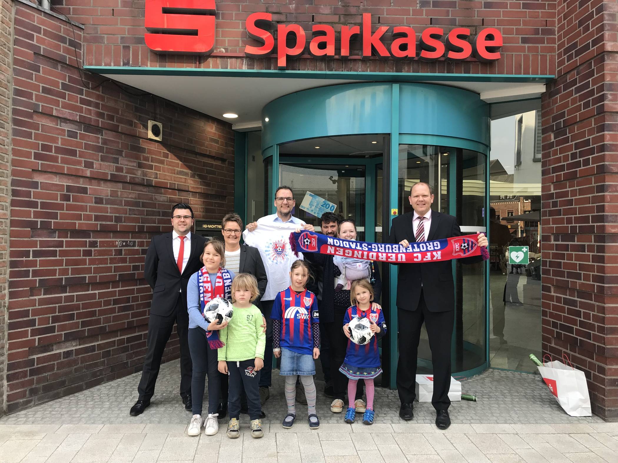  Beim Oster-KFC-Gewinnspiel der Sparkasse Krefeld haben zwei Willicher Familien gewonnen. Beide durften sich über ein Fan-Paket mit Schal, T-Shirt, unterschriebenem Ball sowie einem KFC-Poster mit allen Unterschriften des Teams freuen. Jetzt übergaben Dirk Schumacher, Frau Neis und Herr Dömges von der Sparkasse Krefeld vor dem Finanzcenter Willich die Fan-Pakete an die Familien Kunellis und Greis. 