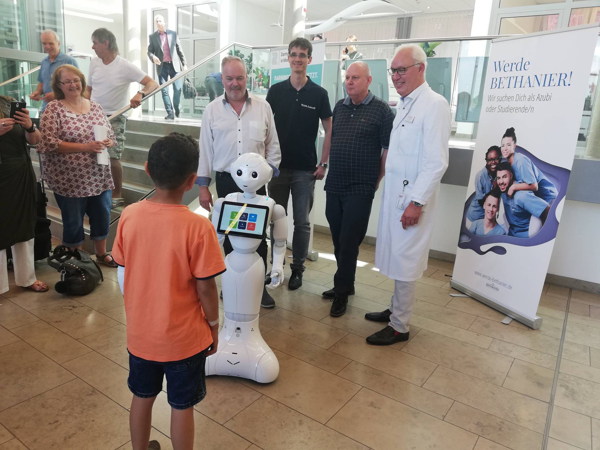  Pepper begrüßt einen kleinen Patienten beim Meet   Greet im Foyer des Bethanien Krankenhauses: Rainer Becker und Matthias Hofmann (beide ShowBotiXX), Ingolf Rascher (Forschungs- und Praxiszentrum humanoide Robotik und KI in Bochum) sowie Dr. Peter Tönnies, Chefarzt der Frauenklinik und Mitglieder der AG Robotik, stellten den Roboter vor, entkräfteten unrealistische Bedrohungsszenarien und erklärten, wie der Roboter in der Praxis Pflegekräfte unterstützen kann. 
