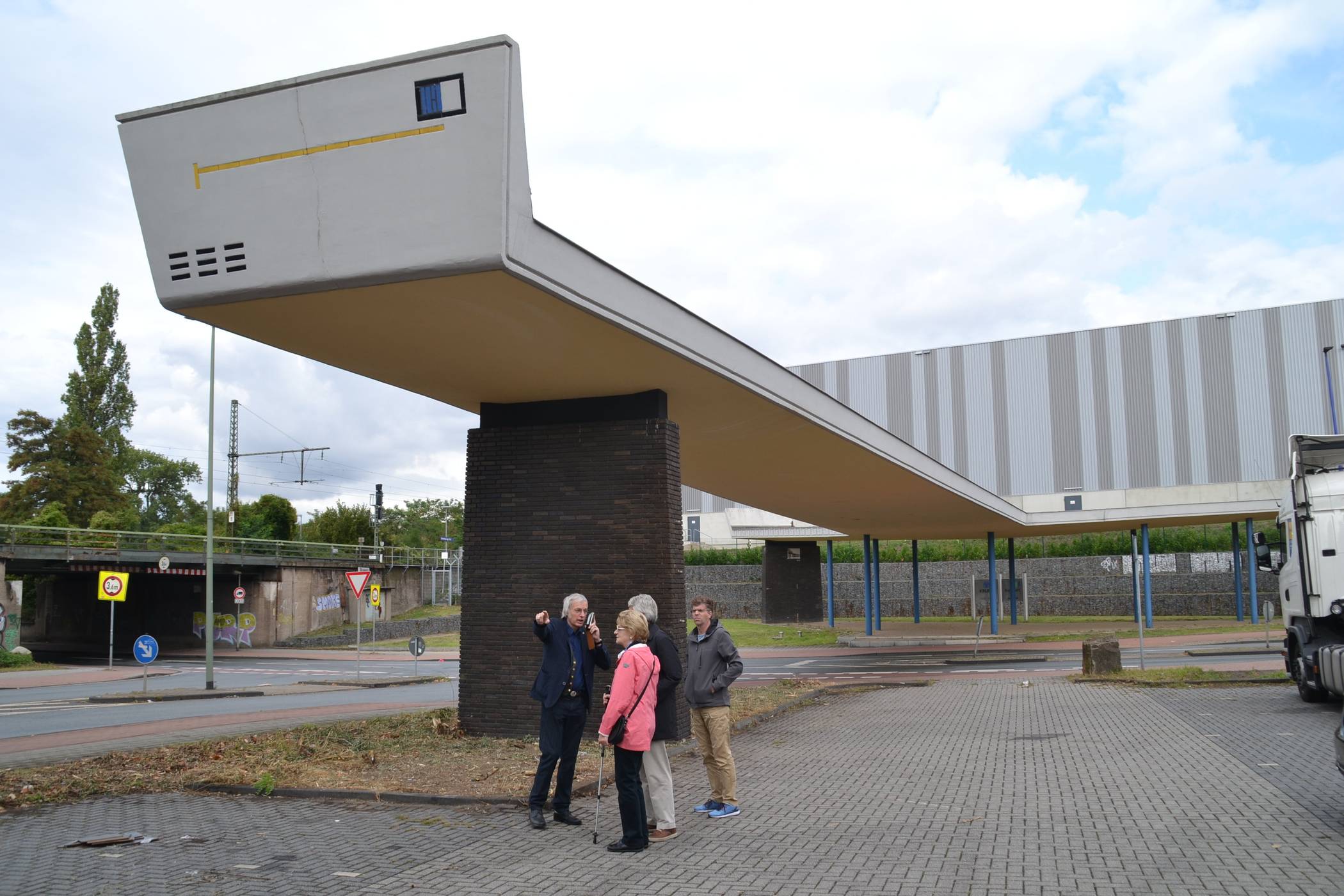  Arno Gollner (l) begleitete einige Interessierte nach dem Vortrag noch zum „TOR 1“. Zwar wurde im Vorfeld des Denkmaltages schnell mit Grün-Schnitt für etwas Ordnung gesorgt, aber insgesamt zeigte sich ein dem Denkmal unwürdiges Erscheinungsbild. Nicht nur, dass das Areal ungepflegt sowie mit Kot diverser Herkunft und Plastikmüll verschandelt ist, auch das Baudenkmal selbst bedarf zeitnaher Pflege, will man es denn wirklich erhalten. Offenkundige Bauschäden müssen gutachterlich untersucht werden. 