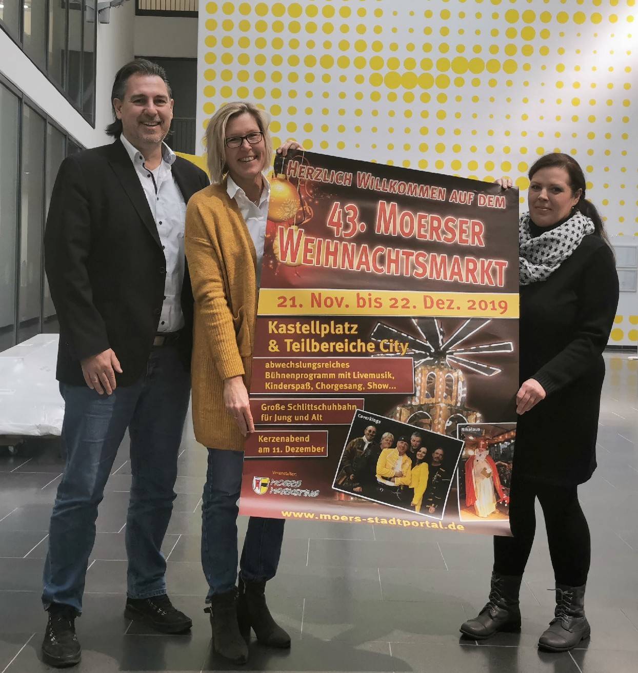 Michael Birr, Sabine Opgen-Rhein (beide MoersMarketing) päsentieren gemeinsam mit Julia Voth (Organisation des Seniorenwunschbaums das Weihnachtsmarkt-Plakat.
