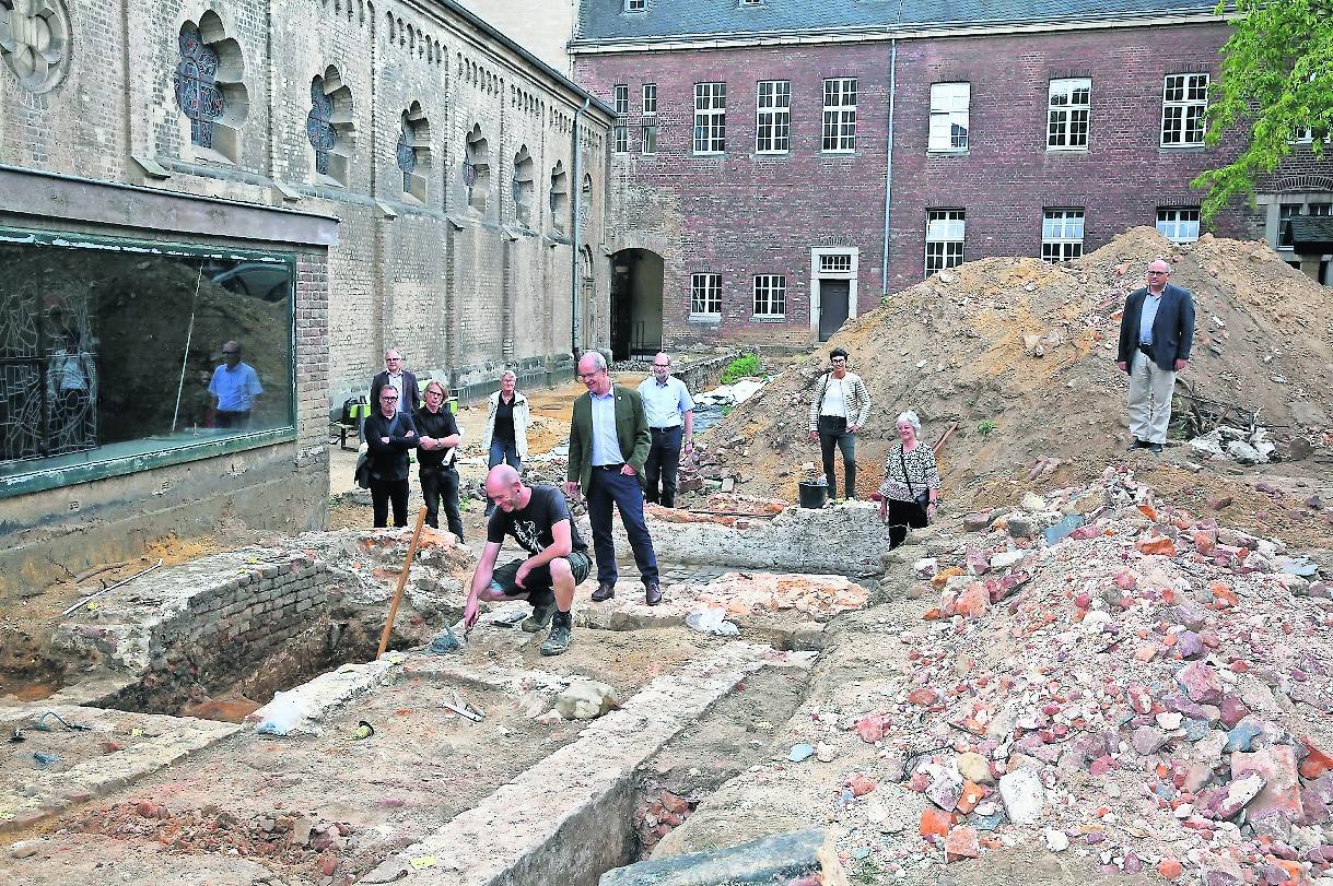  Archäologe Dáire Leahy (knieend) zeigt Oberbürgermeister Hans Wilhelm Reiners im Brunnenhof die Mauerreste des alten Kreuzgangs. Mit im Bild: Die beteiligten Architekten, Mitglieder des Münsterbauvereins und des Kirchenvorstandes. 
